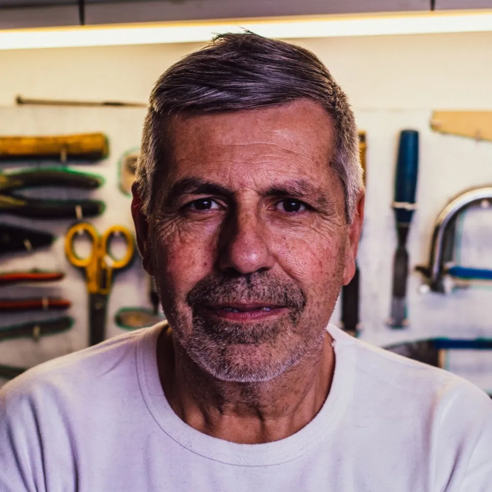 The owner in a plain white tee, tools on the wall behind him