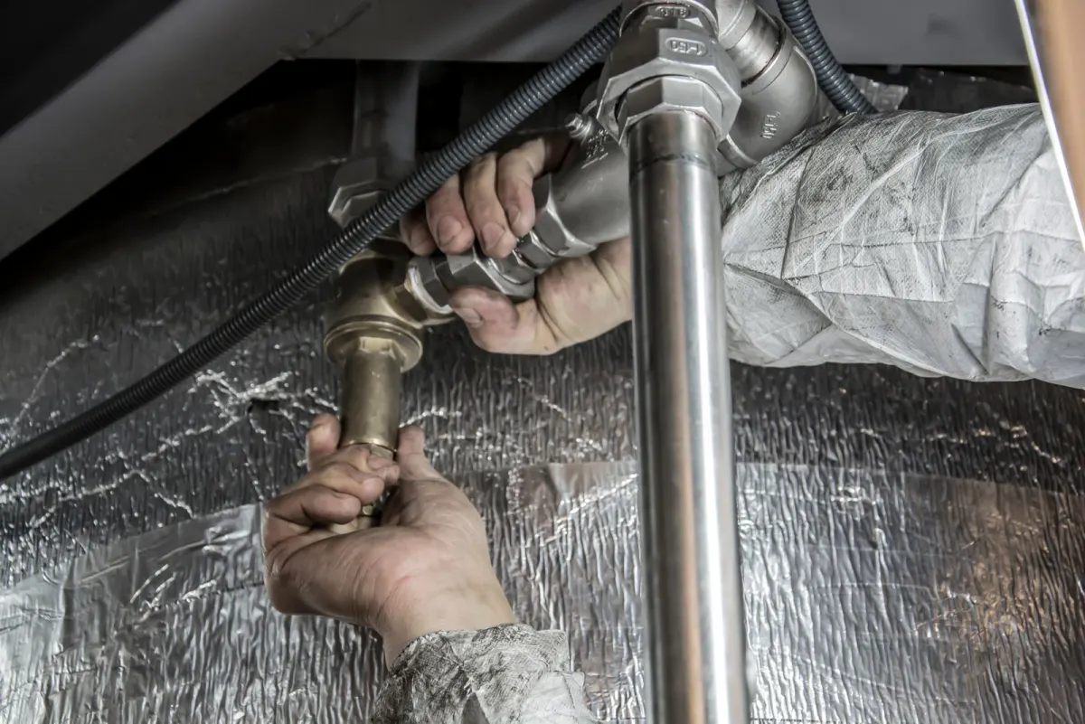 A plumber's hands tightening a brass fitting on a supply line